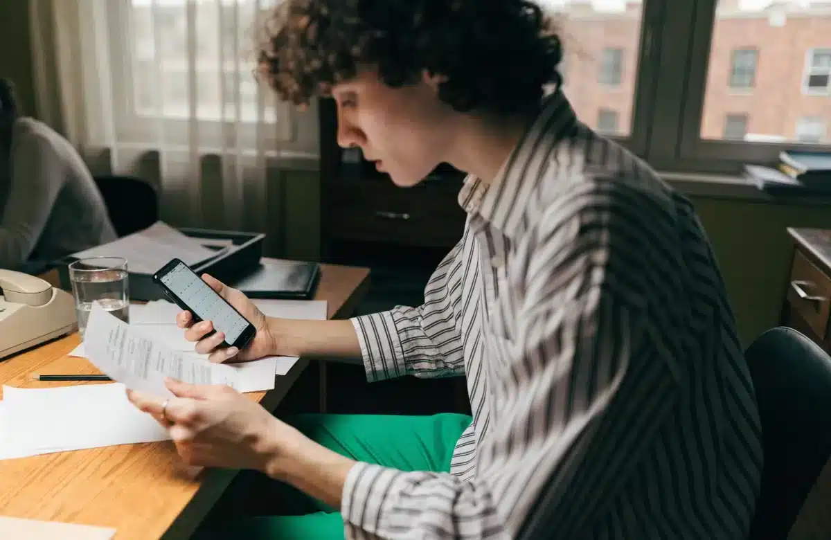 Employee reviewing a paycheck stub and phone calendar at a home desk